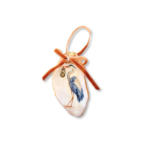 Decoupage oyster shell ornament with a standing blue heron carrying a small ornament, gilded rim, and copper velvet ribbon by Melissa Fouts.