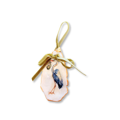 Decoupage oyster shell ornament with a standing blue heron carrying a small ornament, gilded rim, and sage velvet ribbon by Melissa Fouts.