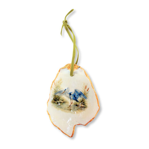 Decoupage oyster shell ornament with a blue heron opening its wings over water on a green ribbon by Melissa Fouts