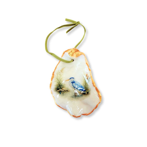 Decoupage oyster shell ornament with a blue heron standing in marsh water on a green ribbon by Melissa Fouts
