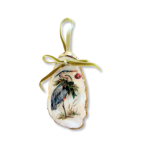 Decoupage oyster shell ornament with a blue heron among holly holding a red ornament, gilded rim, and sage velvet ribbon by Melissa Fouts.