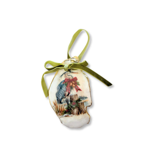 Decoupage oyster shell ornament with a blue heron beside a dock post hung with Christmas bells, gilded rim, and sage velvet ribbon by Melissa Fouts.