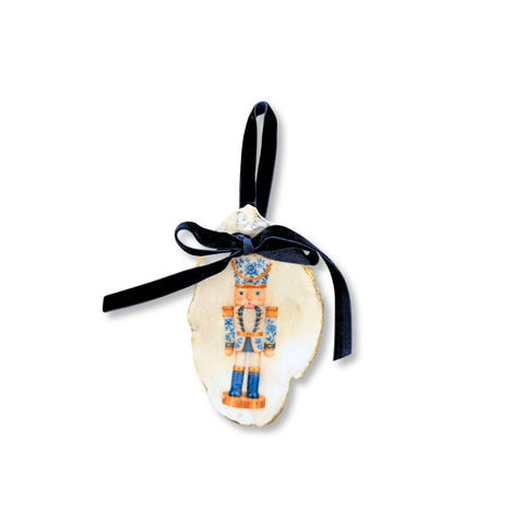 Decoupage oyster shell ornament with a blue-and-white chinoiserie nutcracker on a notched shell, gilded rim, and navy velvet ribbon by Melissa Fouts.