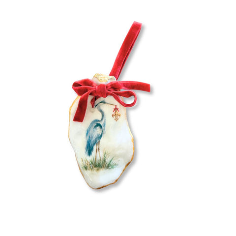 Decoupage oyster shell ornament with a blue heron in a Santa hat holding a fleur-de-lis, gilded rim, and red velvet ribbon by Melissa Fouts.